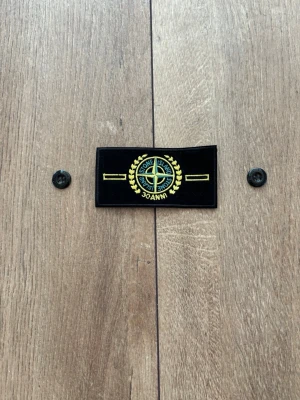 Stone Island Patch / Badge – Limited Edition 30 Anni & knappar - Säljer en limiterad Stone Island-badge med texten "30 Anni" och tillhörande originalknappar, precis som på bilderna. Patchen är helt ny, oanvänd och i perfekt skick. En unik jubileumsmodell som passar perfekt som samlarobjekt eller reservdel till din jacka/tröja. 
