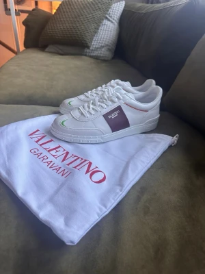  Valentino Garavani open sneakers - Snygga vita sneakers från Valentino Garavani med gröna och röda detaljer samt en brun panel på sidan. Skorna har klassisk låg siluett, vita snören och är tillverkade i slätt läder. Perfekta för dig som vill ha en clean och exklusiv look.
