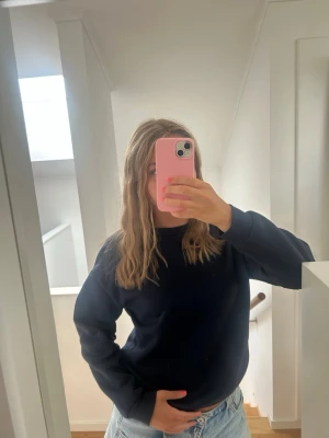 Mörkblå sweatshirt i basic stil - En enkel och stilren mörkblå sweatshirt med rund hals och långa ärmar. Tröjan har en avslappnad passform och är perfekt att matcha med jeans eller andra casual plagg. Materialet ser ut att vara mjukt och bekvämt, troligen bomull eller bomullsblandning.