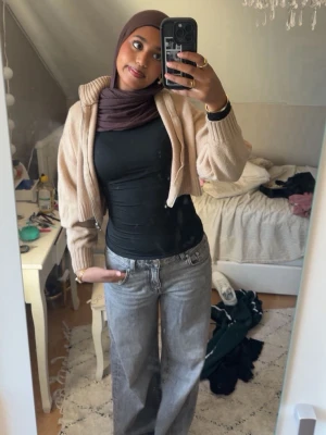 Beige cropped kofta med dragkedja - Säljer en beige cropped kofta med dragkedja framtill och ribbade muddar vid ärmslut och krage. Koftan har en avslappnad passform och är perfekt att slänga över en topp. Materialet ser ut att vara mjukt och stickat, vilket ger en mysig känsla.
