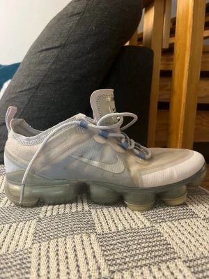 Nike Air Vapormax Limited edition 2017 vita sneakers  - Nike Air Vapormax sneakers i vitt och ljusgrått med transparent mesh-överdel och tydlig synlig Air-sula. Skon har vita och ljusblå detaljer på snörningen samt en modern, sportig look. Perfekt för dig som gillar streetwear och komfort 10/10 skick passar strl 40 bra med enligt mig pris kan diskuteras.
