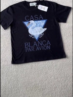 Svart t-shirt med svanmotiv - Cool svart t-shirt med tryck av en vit svan och texten 'Casa Blanca Par Avion' framtill. T-shirten har rund hals och korta ärmar. Perfekt för dig som gillar grafiska motiv och vill sticka ut lite extra.