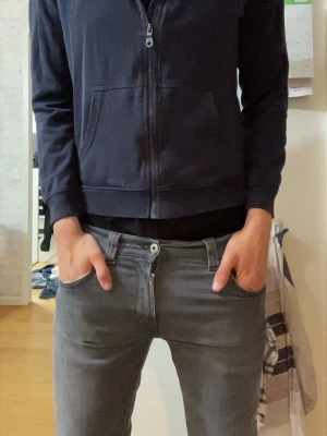 Mörkblå hoodie med dragkedja lyle & scott - Snygg mörkblå hoodie med dragkedja och huva. Framtill finns två fickor och ett litet gult broderat märke på bröstet. Perfekt för en avslappnad stil och enkel att matcha med jeans eller joggers.