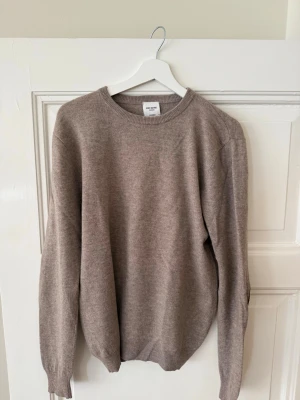 Beige cashmeretröja John Henric - Mjuk och stilren beige stickad tröja från John Henric i 100% cashmere. Rund halsringning och ribbade muddar vid ärmslut och nederkant. Perfekt för dig som gillar klassisk och enkel stil.