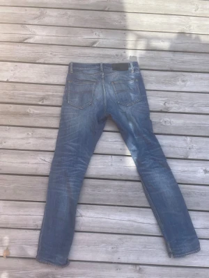Blå raka jeans med slitningar - Säljer ett par klassiska blå jeans med raka ben och snygga slitningar framtill. Jeansen har fem fickor, normal midja och är gjorda i denim. Perfekta för en avslappnad och trendig look.