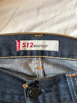 Levi's 512 Bootcut jeans blå - Säljer ett par klassiska Levi's 512 Bootcut jeans i mörkblå denim. Jeansen har fem fickor, orangea kontrastsömmar och knappgylf. Bootcut-modellen ger en snygg siluett och passar perfekt till sneakers eller boots. Hör av er vid minsta lilla fundering😊 