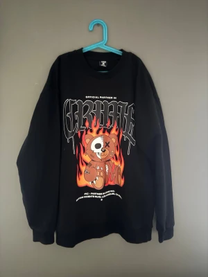 Svart sweatshirt med björntryck FSBN - Cool svart sweatshirt från FSBN i relaxed fit med stort tryck av en tecknad björn och eldflammor på framsidan. Rund halsringning och långa ärmar. Perfekt för dig som gillar streetwear och grafiska prints. Tröjan har även ett litet märke där på sidan, men inget man tänker på hör av er vid minsta fundering elller tanke om pris😃✅👍