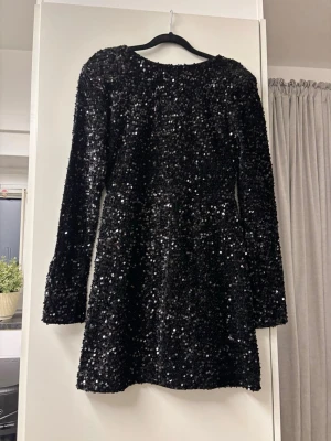 BikBok Svart Paljettklänning Öppen Rygg Ny M)  - Helt ny paljettklänning från Bik Bok – modell "DK Vega"! ✨ Snygg svart kort klänning täckt med glittrande paljetter, långa ärmar och en djup öppen rygg med ett fint knytband upptill. Perfekt för fest, nyår eller klubbkvällar!  Märke: Bik Bok  Modell: DK Vega  Storlek: M  Färg: Svart  Skick: Helt ny och oanvänd med alla prislappar kvar (Nypris: 599 kr).  Detaljer: Långärmad, rundad hals framtill, öppen rygg med satinknytningsband. 