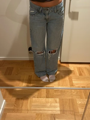 Ljusblå slitna Levi's jeans - Säljer ett par ljusblå Levi's jeans med raka ben och stora slitningar vid knäna. Klassisk femficksmodell med Levi's patch bak och röd etikett på fickan. Perfekta för en avslappnad och trendig look.