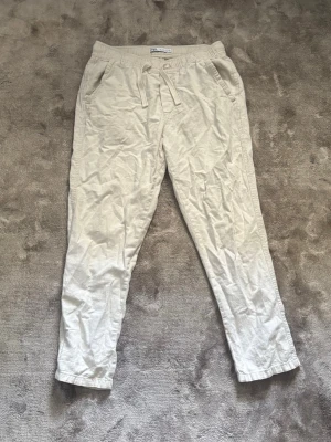 Beiga linnebyxor  - Snygga och avslappnade beiga linnebyxor med dragsko i midjan och sidofickor. Byxorna har en rak passform och är perfekta för en chill och stilren look. Tillverkade i ett lätt och luftigt linnematerial som passar perfekt till sommaren.
