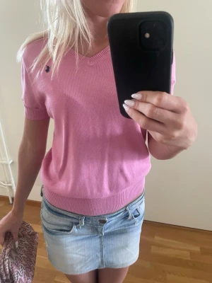 Rosa kortärmad tröja från Polo by Ralph Lauren  - Snygg rosa tröja med v-ringning och korta ärmar. Tröjan har ribbade muddar vid ärmslut och nederkant samt en liten broderad logga på bröstet. Passar storlek xs samt S! Jag köpte den på Plick och fick den med svarta stygn på insidan av ena ärmen som kan ses på sista bilden, men det är inget man ser med tröjan på! Tveka inte att höra av er om frågor eller prisförslag!