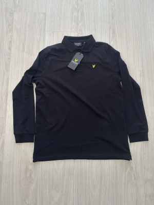  Lyle & Scottlångärmad pike - Klassisk svart långärmad pikétröja från Lyle & Scott med gul broderad logga på bröstet.  Köpt ifrån kidsbrandstore för 900kr och är helt ny och oanvänd perfect för sommaren  man har den grisch/laidback stilen !