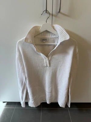 Vit stickad tröja från Lardini, Stl 42/M - Klassisk vit stickad tröja från Lardini med ribbad krage och knappslå framtill. Tröjan har långa ärmar och ribbade muddar vid ärmslut och nederkant. Perfekt för en stilren och avslappnad look.