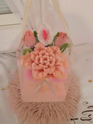 Dekorativ blomsterbukett i box - Säljer en söt dekorationsbukett med handgjorda blommor i mjuka pastellfärger. Blommorna är gjorda av piprensare i rosa, vitt och grönt, och står i en ljusrosa box med transparent lock. Perfekt som prydnad på skrivbord eller hylla. Eller som en present till någon du tycker om!