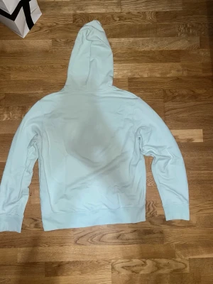 Ljusblå hoodie från A.P.C - Ene stilren ljusblå hoodie med huva och dragsko. Tröjan har ribbade muddar vid ärmslut och nederkant samt en klassisk passform. Perfekt för en avslappnad look och enkel att matcha med jeans eller joggers.