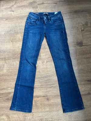 Blå bootcut jeans med låg midja - Snygga blå bootcut jeans med låg midja och klassiska fem fickor. Jeansen har en lätt tvättad look och raka ben som blir vidare nedtill. Perfekta för en avslappnad och trendig stil. Stängs med dragkedja och knapp framtill.