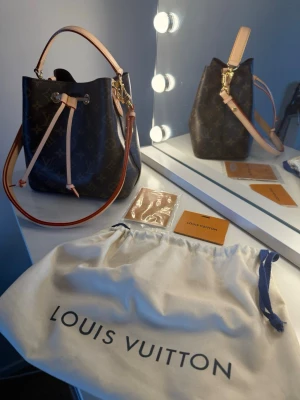 Monogram handväska - Säljer en klassisk handväska i mörkbrunt monogrammönster med ljusa läderdetaljer och guldfärgade metalldelar. Väskan har både axelrem och handtag samt dragskostängning. Dustbag och tillbehör medföljer.