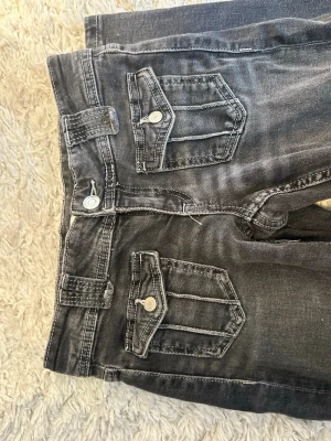 Grå jeans med ficklock och kontrastsömmar - Säljer ett par grå jeans med coola ficklock och vita kontrastsömmar. Jeansen har raka ben, breda hällor och detaljerade fickor både fram och bak. Materialet är klassisk denim i bomull med en tvättad look.