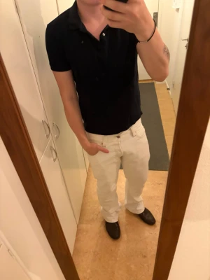 Svart piké med krage och knappar - Snygg svart pikétröja med klassisk krage och knappar framtill. Tröjan är kortärmad och har en normal passform, perfekt för en clean och enkel stil. Passar till både jeans och chinos.