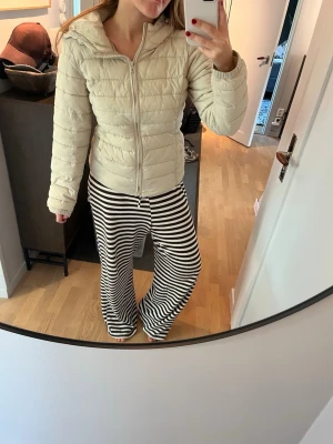 Beige pufferjacka med huva - Säljer en beige pufferjacka med huva och dragkedja framtill. Jackan har quiltad design, långa ärmar och elastiska muddar vid ärmsluten. Den är ifrån Only och i storlek M 