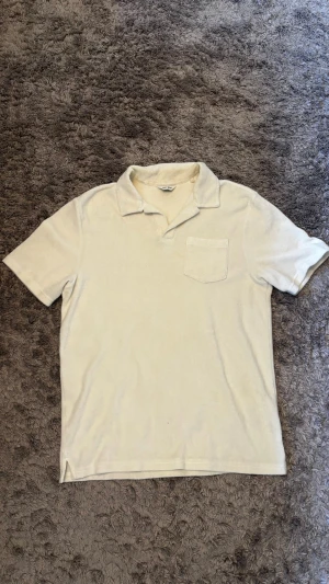 Vit frotté polotopp från East West - Klassisk vit polotopp från East West i mjuk frotté. Toppen har korta ärmar, krage och en bröstficka för extra stil. Perfekt för dig som gillar en clean och enkel look med en twist av retrokänsla.