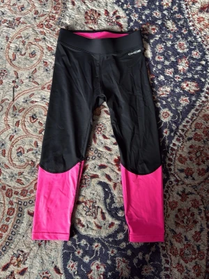 Svarta och rosa löpartights XLO Running - Snygga löpartights från XLO Running i svart med knallrosa ben. Tightsen har bred resår i midjan och reflekterande detaljer baktill. Tillverkade i stretchigt funktionsmaterial som passar perfekt för träning och löpning.