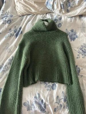 Grön croppad stickad polotröja - Mysig grön stickad polotröja med croppad passform och bred ribbad kant vid ärmslut och nederkant. Perfekt för lager på lager och ger en trendig look till din outfit.