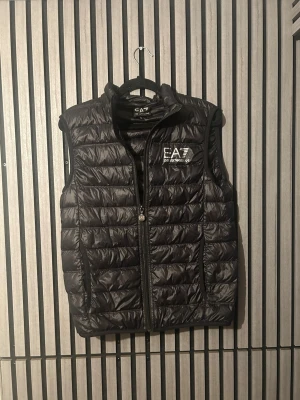 Svart dunväst från EA7 Emporio Armani - Snygg svart dunväst från EA7 Emporio Armani inga håll dock står står de namn i den. Pris kan diskuteras 