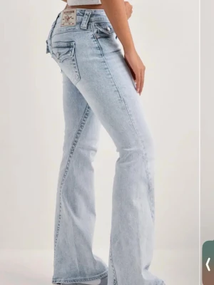 True religion ljusblå bootcut jeans med fickdetaljer - Säljer ett par ljusblå bootcut True religion jeans med snygga fickdetaljer bak och klassisk femficksdesign. Jeansen har lågmidjad och utsvängda ben, vilket ger en retroinspirerad look.Tillverkade i denim med en tvättad finish för en avslappnad vibe. Pris kan diskuteras och skriv för mer bilder