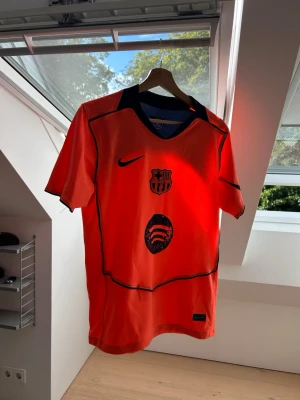 Barcelona orange matchtröja Nike - Snygg orange FC Barcelona matchtröja från Nike med klubbmärke och Spotify-logga på bröstet. Tröjan har svarta detaljer, korta ärmar och V-ringad krage med mörkblå inslag. Perfekt för dig som älskar fotboll och vill sticka ut på planen.