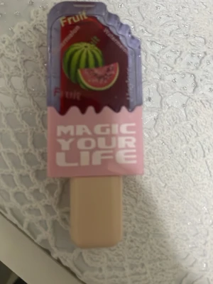 Vattenmelon läppbalsam i glassform - Sött läppbalsam utformat som en glass med vattenmelonmotiv och texten 'MAGIC YOUR LIFE' på framsidan. Färgerna är lila, rosa och beige. Perfekt för dig som gillar roliga och unika skönhetsprodukter.