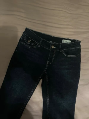 Mörkblå bootcut jeans med en dekorations fika på ena sida fram - Ett par lågmidjade jeans ifrån Only, helt oanvända köpte nyligen men kommer inte till användning 💕
