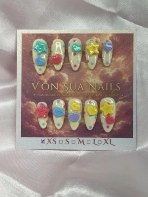 CandyPop 🍭(XS);Medium Almond - Handgjorda press-on naglar i en medium lång almondform med pastellfärgade handgjorda 3D-dekorationer som stjärnor, hjärtan i blått, gult, rosa och turkost. Basen är ljus med färgglada prickar. Perfekt för dig som vill ha en lekfull och unik nagelstil.XS: 14 mm, 11 mm, 11,5 mm, 10 mm, 8 mm