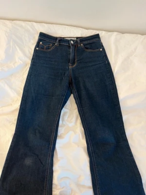 Mörkblå bootcut jeans Stradivarius - Snygga mörkblå bootcut jeans från Stradivarius med klassiska fem fickor och kontrastsömmar. Jeansen har hög midja och utsvängda ben, vilket ger en trendig siluett. Tillverkade i ett mjukt denimtyg som sitter bekvämt hela dagen.