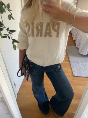 Paris stickad tröja - Mysig vit tröja med beige texten 'PARIS' framtill. Tröjan har en avslappnad passform, ribbade muddar och är tillverkad i ett mjukt, fluffigt material. Perfekt för dig som gillar en enkel men trendig stil.