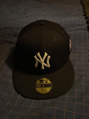Svart New Era Yankees keps - Snygg svart New Era 59FIFTY keps med New York Yankees-logga broderad framtill och World Series-märke på sidan. Klassisk flat brim och strukturerad passform. Perfekt för dig som gillar streetwear och sportig stil.
