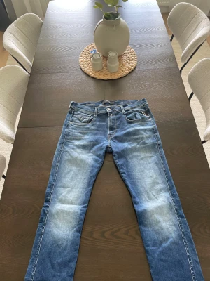 Blå Replay jeans med slitningar - Säljer ett par blå jeans från Replay med snygga slitningar och tvättade detaljer. Modellen har klassisk femficksdesign, normal midja och smal passform. Materialet är stretchigt för extra komfort. Perfekta för en avslappnad och trendig look.