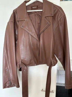 Brun skinnjacka från Bianca x Nelly - Snygg brun skinnjacka från Nelly.com  tidigare kollektion med Bianca Ingrosso🤎 Jackan har en bikerdesign, bred krage, dragkedja och bälte i midjan. Jackan har detaljerade sömmar och dragkedjor vid ärmsluten för extra edge. Storlek 38.