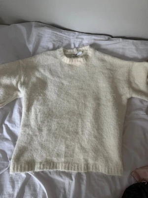 Krämvit stickad tröja med rund hals - Mysig krämvit stickad tröja med rund hals och långa ärmar. Tröjan har en enkel och stilren design med ribbstickade muddar vid ärmslut och nederkant. Perfekt för lager-på-lager och passar till det mesta i garderoben.