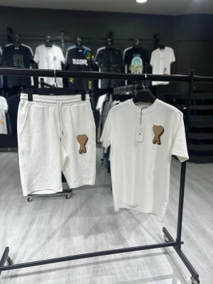 Vitt set med brunt hjärtmärke - Snyggt vitt set med t-shirt och shorts, båda med ett brunt hjärtmärke på vänster sida. T-shirten har rund hals och korta ärmar, shortsen har resår i midjan och sidofickor. Perfekt för en avslappnad och trendig look.