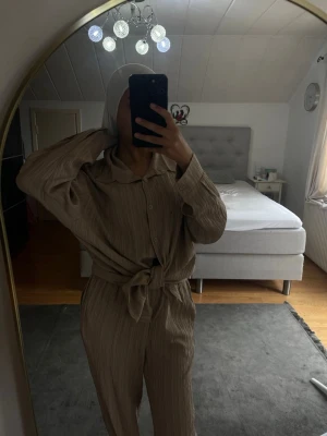 Beige ribbad loungewear-set - Säljer ett beige loungewear-set med ribbad struktur. Setet består av en långärmad skjorta med krage och knappar framtill samt matchande byxor med hög midja och knytband i midjan. Perfekt för chill dagar hemma eller när du vill vara bekväm men ändå se snygg ut. Finns några fläckar men går bort 