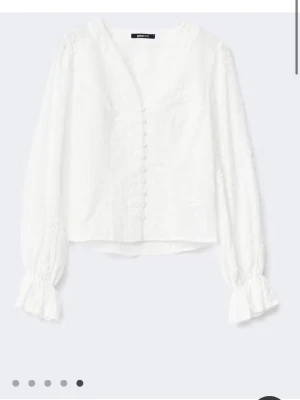 Vit blus - Stilren vit blus med v-ringning och broderade blommor. Blusen har långa ärmar med volang vid ärmslut.