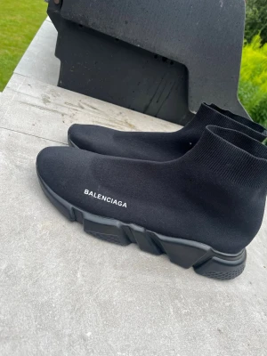 Svarta springskor - Säljer ett par svarta  Speed sneakers med strumpliknande ovandel och chunky sula. Skorna har vit logga på sidan och är tillverkade i stretchigt syntetmaterial för en clean och modern look.