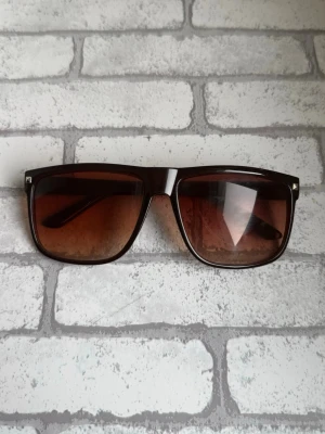 Rayband liknande solglasögon  - Snygga solglasögon med stora, fyrkantiga bågar i mörkbrunt plastmaterial och bruna tonade glas. Perfekta för soliga dagar och ger en cool retrovibe till din outfit.