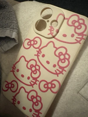 Shein iPhone 16 Hello Kitty mobilskal - Snyggt beige mobilskal med flera rosa Hello Kitty-motiv. Från shein jag andvänder då inte den här mobilskalet då jag inte tycker den passar till min mobil 