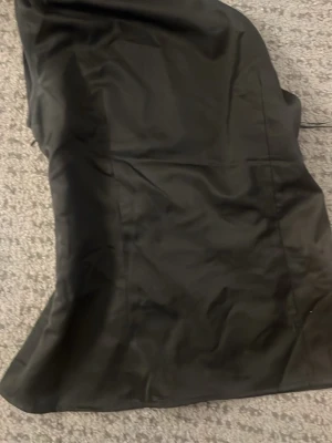 Svart axelbandslös blus med knappar - Snygg svart axelbandslös blus med guldfärgade dekorativa knappar vid bysten. Blusen har en enkel, elegant siluett och är gjord i ett slätt material som ger en stilren look.