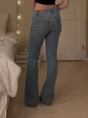 Bootcut jeans - Säljer ett par snygga ljusblå bootcut jeans i midwaist med slitning på ena knät. Jeansen är tillverkade i denim med en snygg tvätt. Säljer då de inte längre passar mig💗 slitna längst ned på benen, syns på sista bilden💗