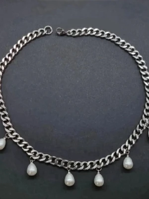 Kedjehalsband med pärlor - Snyggt halsband i silverfärgad metall med grov kedja och droppformade vita pärlor som hänger längs hela halsbandet. Perfekt för dig som vill ha en trendig accessoar med lite extra edge och pärldetaljer.
