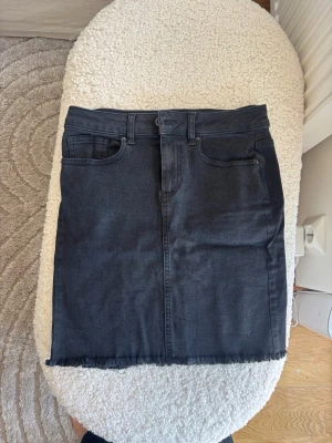 Svart jättefin jeanskjol - Säljer en jeanskjol med fem fickor och rå, fransad kant nedtill. Kjolen har klassisk jeanslook med bälteshällor och knappstängning framtill. Perfekt till vardags för en avslappnad men snygg stil.