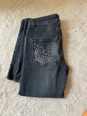 Mörkgrå jeans med färgglada nitar - Snygga mörkgrå jeans från ONLY med färgglada nitar på fickor och ben. Jeansen har klassisk femficksmodell, normal midja och smal passform. Materialet är stretchigt denim som sitter bekvämt hela dagen. Perfekta för dig som vill ha något extra i vardagslooken.